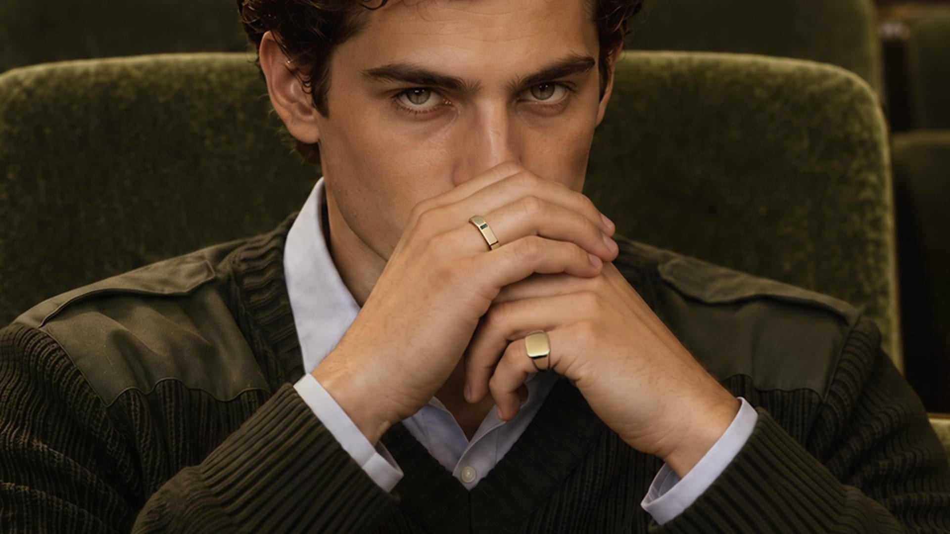 Miansai gold tone rings worn on the fingers with one rectangular signet ring visible near the face