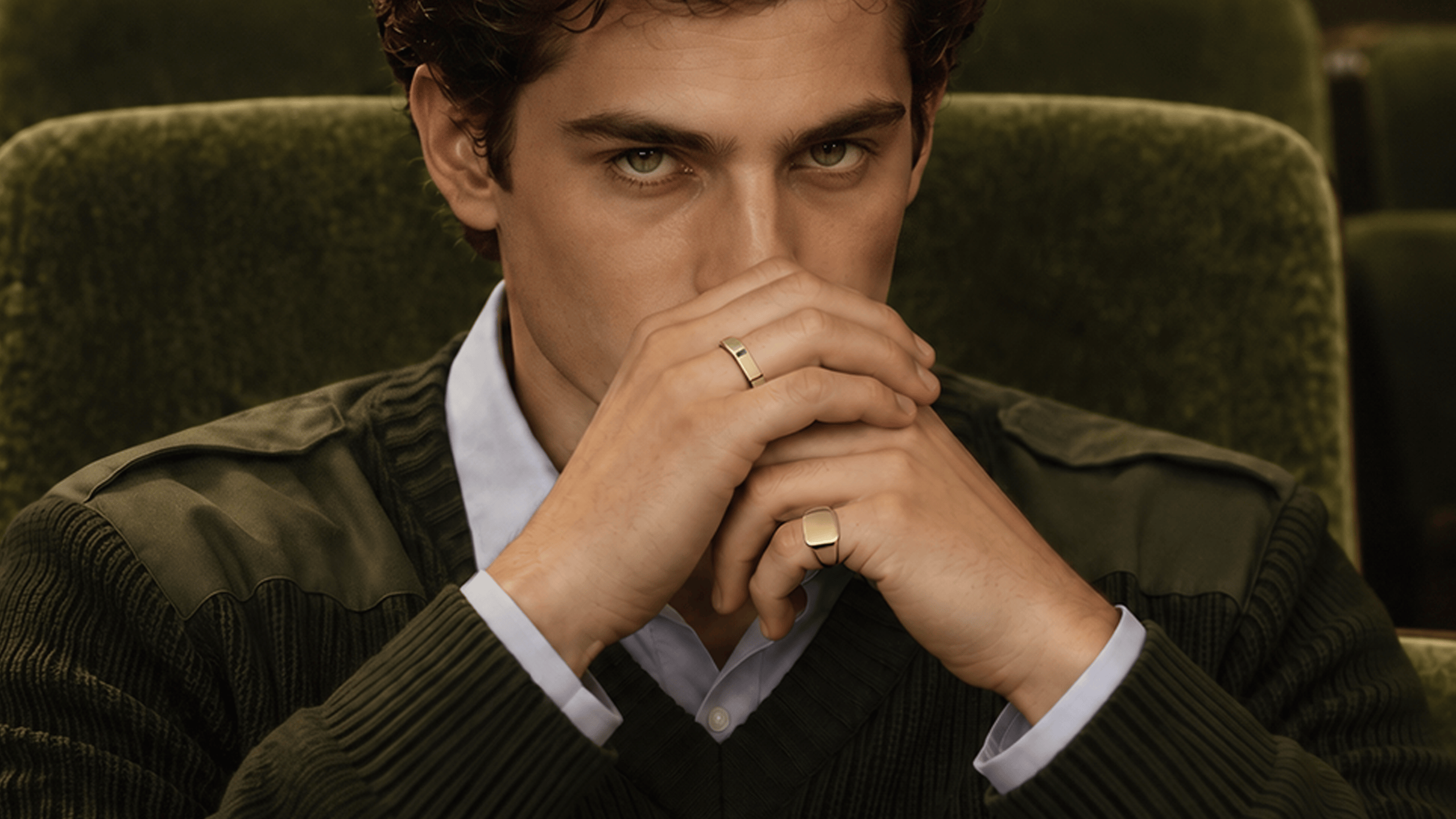 Miansai gold tone rings worn on the fingers, featuring a slim band and a square signet face near the model's face