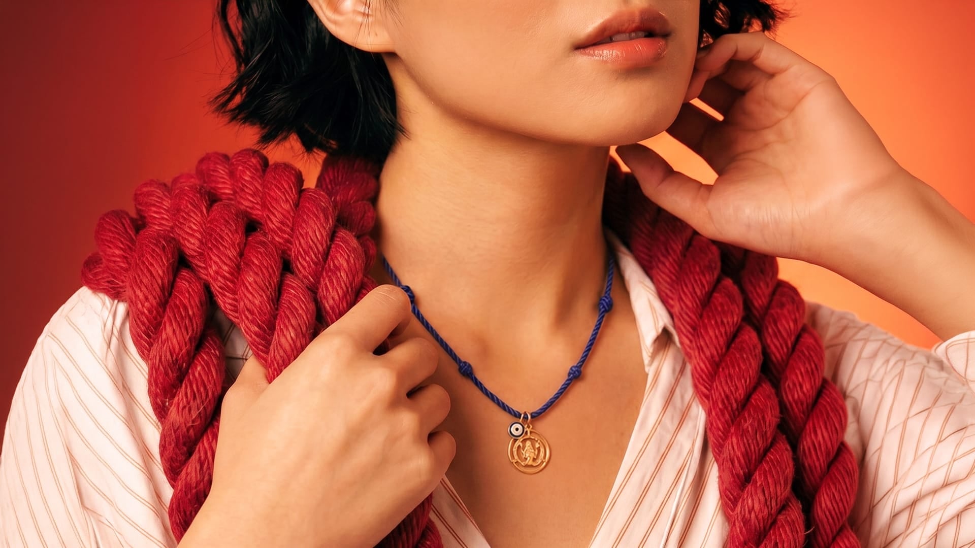 Person wearing a red knitted scarf and blue necklace with a pendant against an orange background