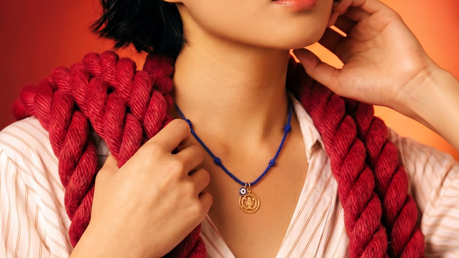 Person wearing a red knitted scarf and blue necklace with a pendant against an orange background