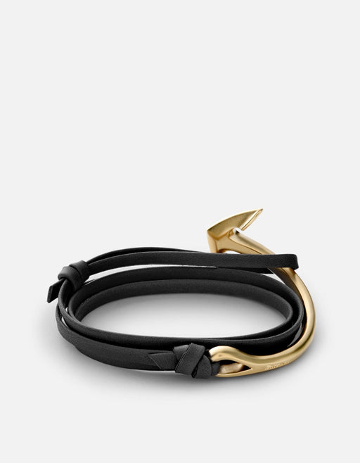 Miansai black leather half-cuff bracelet with a matte gold-plated anchor closure, fastened in an open curve