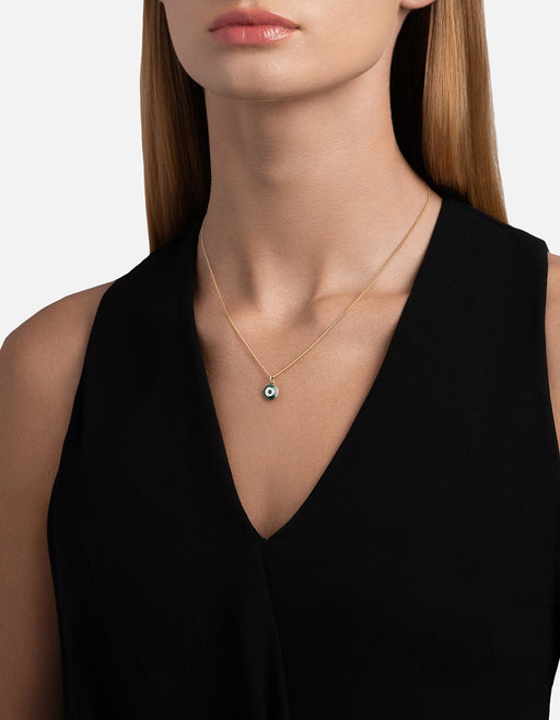 Miansai Ojos pendant necklace in gold vermeil with a green enamel evil eye worn at the neck over a black sleeveless V neck top