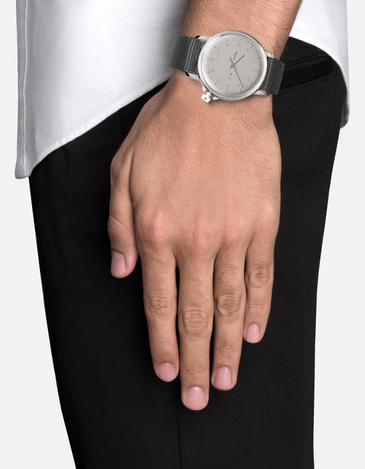 Miansai M12 Swiss watch in stainless steel with a pale gray dial and woven gray nylon strap worn on the wrist