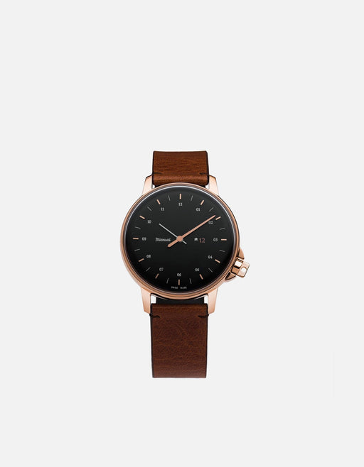 Miansai M12 Swiss watch with a rose tone stainless steel case, dark dial, and brown cognac leather strap